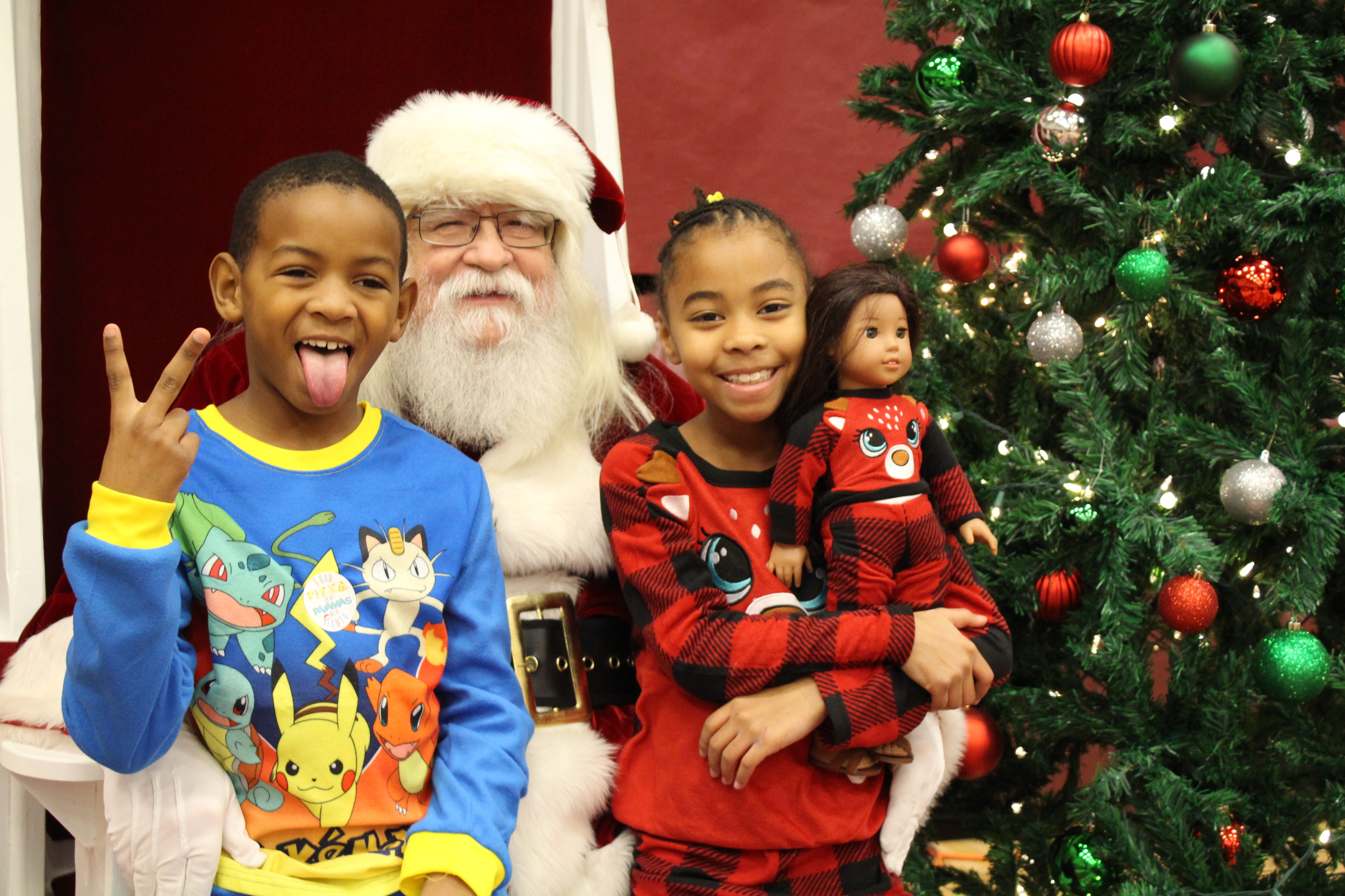 2 smiling children dressed in pajamas sitting on Santa's lap