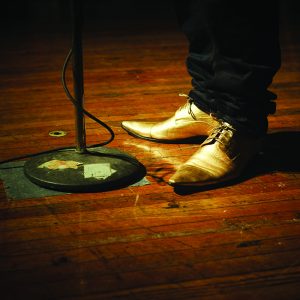 shiny gold shoes standing on worn hardwood floors with microphone stand.