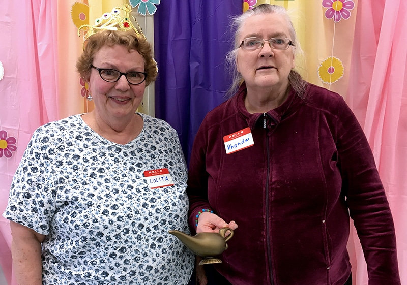 2 older ladies smiling with a crown and "magic lamp"
