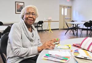 Older woman sitting at table coloring with a marker in her hand.
