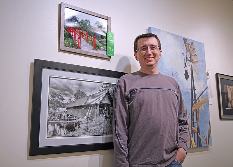 Man proudly standing in front of framed artwork on the wall.