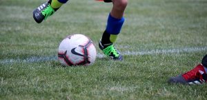 close shot of Nike Soccer ball being kicked by youth soccer player with black cleats, green laces, and blue shin guards.