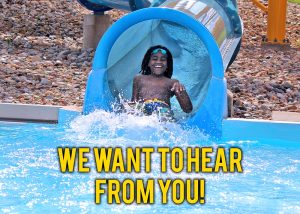 Boy making a big splash at the end of a water slide. Text reads: We Want to hear from you!
