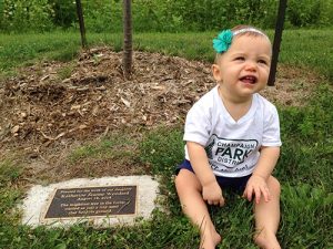 Baby sitting up next to plaque of her own Grow with me Tree