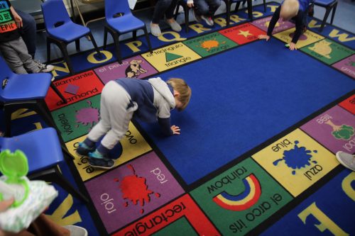 A small child crawls on a colorful rug.