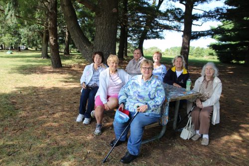 A group of older people sitting outside at a picnic table.