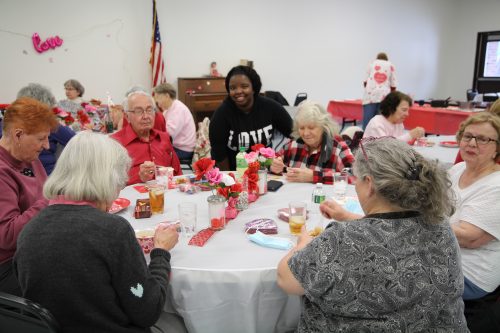 A group of older people eating a meal at a Valentine's Day themed party.