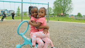 Two young kids sitting on the playground smiling.