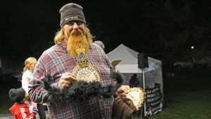 Man with large natural beard holding the overall winner trophy of the Flannel Fest Mustache Contest.