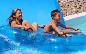 Two kids smiling going down a large water slide using a tandem innertube. 