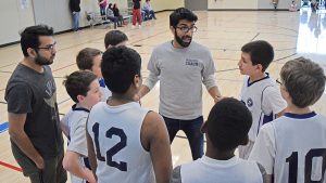 Volunteer Coach instructing youth basketball team during a timeout.