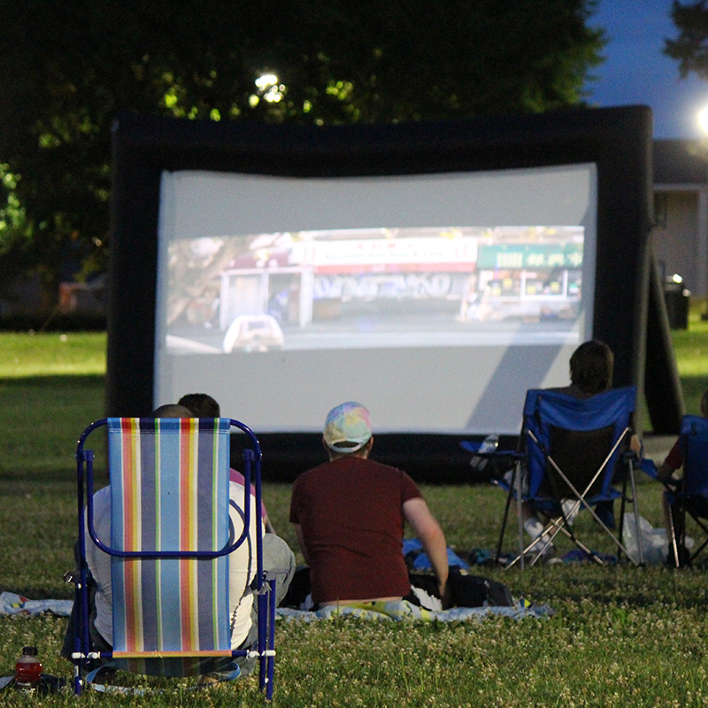 Group of people watching a movie on a big screen in the park.