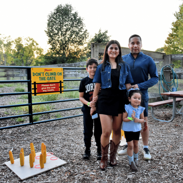 A family of four poses in front of a horse pasture with a game of ring toss next to them.