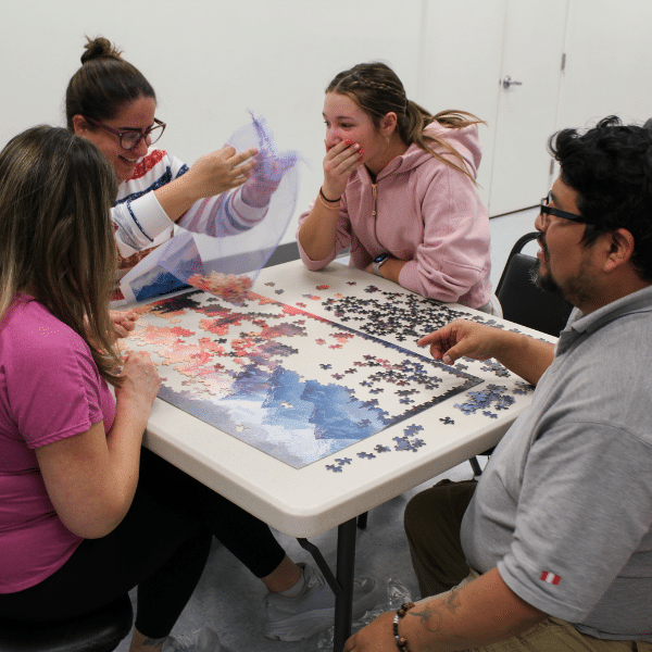 Four adults sit around a table and solve a puzzle