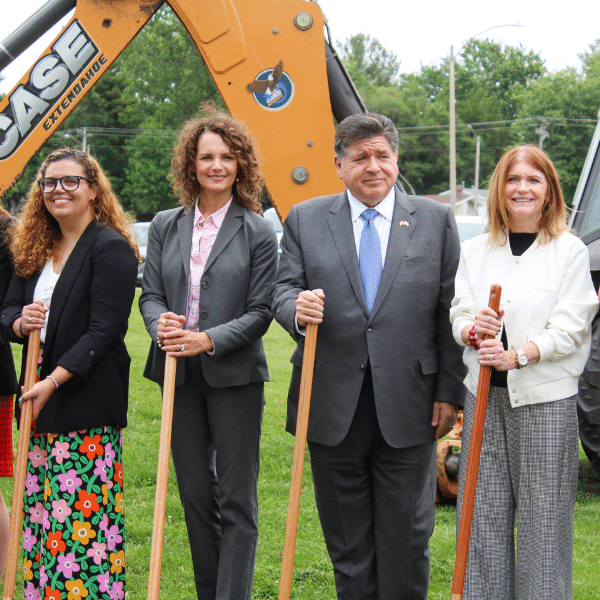 Four adults hold shovels to break ground for a construction project.
