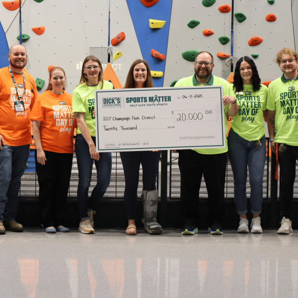 A group of adults hold a large check in front of a rock-climbing wall.