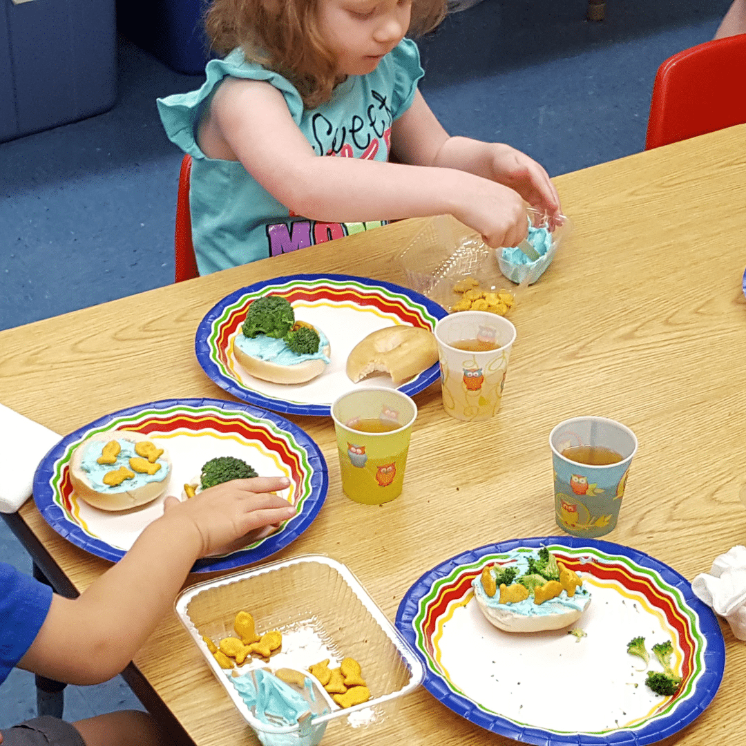Children sit around a table decorating bagels.