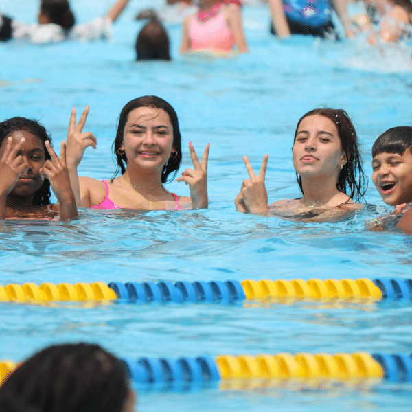Four teens pose with peace signs in a pool.