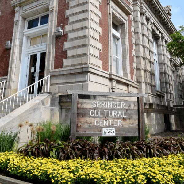 A wooden sign sits in a bed of yellow flowers and reads, "Springer Cultural Center."